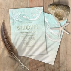 two wedding cards on top of a wooden table next to a seashell and starfish