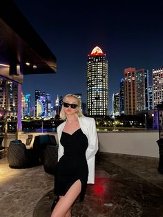 a woman in a black dress and white blazer posing for the camera at night