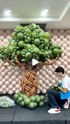 a man sitting on a bench next to a large tree made out of fruits and vegetables