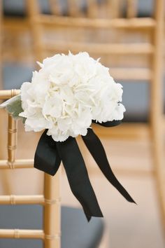 a bouquet of white flowers tied to a wooden chair with black ribbon on the back