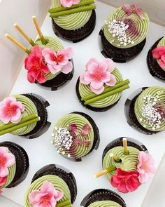 cupcakes decorated with green frosting and pink flowers are on display in a box