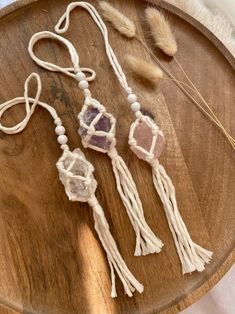 three tassels with beads and feathers on a wooden tray next to a feather