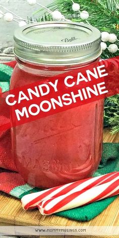 a jar filled with candy cane moonhine sitting on top of a wooden cutting board