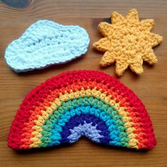 three crocheted hats are sitting on a wooden surface, one has a sun and the other is a rainbow