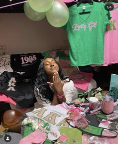 a woman sitting on the floor surrounded by pink and green shirts, balloons and other items