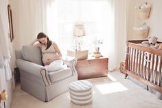 a pregnant woman sitting in a chair next to a baby crib with her hands on her stomach