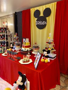 a table topped with lots of cakes and mickey mouse figurines next to a red curtain