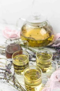 three glasses filled with green tea next to some lavender flowers and a jug of oil