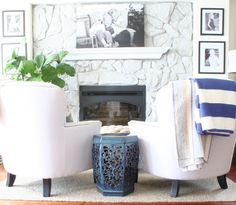 two white chairs sitting in front of a fireplace with pictures on the wall behind them