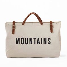 a canvas bag with leather handles and the word mountains printed on it, sitting against a white background