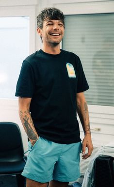 a man with tattoos standing in front of a chair and looking at the camera smiling