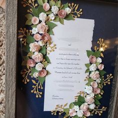 a wedding card with flowers on it in a wooden frame next to a piece of paper