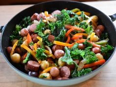 a bowl filled with sausage, broccoli and carrots on top of a wooden table