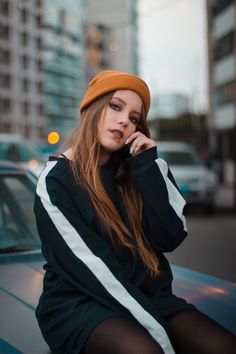 a woman sitting on the hood of a car talking on her cell phone while wearing a beanie