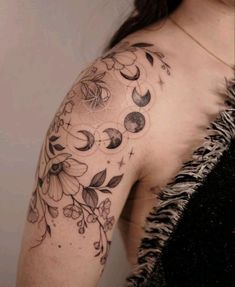 a woman's shoulder with flowers and moon tattoos on her left arm, behind her is a feathery black dress