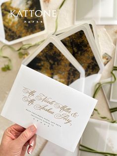 a person holding up a wedding card in front of some other cards on a table