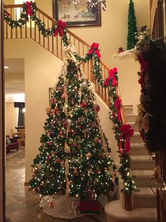 a christmas tree is decorated with red and green bows on the stairs in front of a staircase case