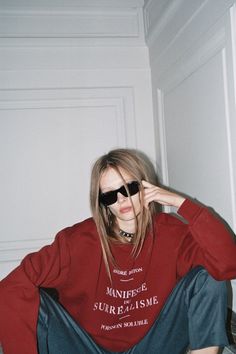 a woman sitting on the floor wearing sunglasses and a red shirt with words written on it