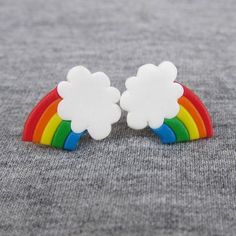 a pair of rainbow and cloud stud earrings on grey fabric background with copy space for text