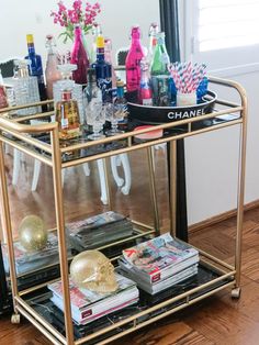 a gold bar cart filled with liquor bottles and other drinks on top of a hard wood floor