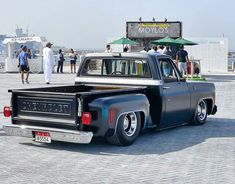 an old black pickup truck parked in front of a building with people standing around it