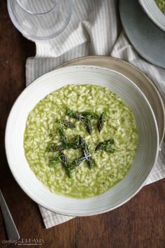 a white bowl filled with green soup on top of a wooden table next to silverware