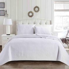 a white bed in a bedroom with two lamps and pictures on the wall behind it