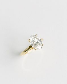 a yellow gold ring with an oval cut diamond in the center on a white background