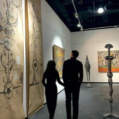 two people are looking at artwork on display in an art gallery, one is holding the hand of another person's hand