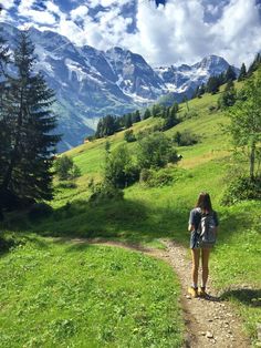 a woman with a backpack is standing on a trail in the mountains looking at the snow - capped peaks