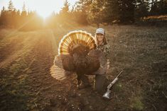 a woman kneeling down with a turkey on her lap in the middle of a field