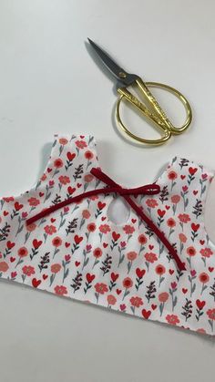 scissors are laying next to a piece of fabric with red flowers on it and a pair of gold scissors