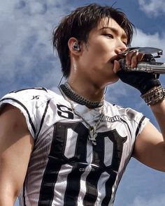 a young man drinking from a water bottle while wearing an american flag shirt and silver bracelets