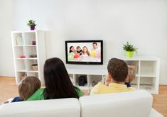 family watching television in their living room with the tv on and two children sitting on the couch