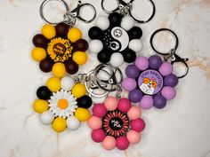 four key chains with different colored beads and flowers on them, sitting on a marble surface