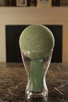 a green ball sitting in a glass vase on a marble counter top next to a fireplace