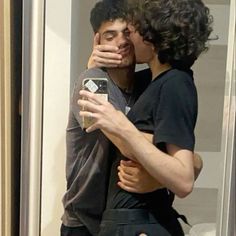 two people are hugging each other while one person is taking a selfie with his cell phone