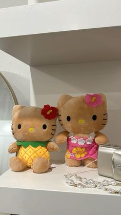 two hello kitty dolls sitting on top of a white shelf next to a silver camera