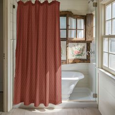 a red shower curtain hanging in front of a white bath tub and window with wooden trim