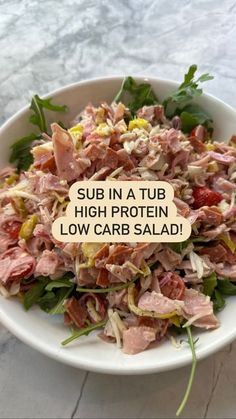 a white bowl filled with salad on top of a marble countertop next to a sign that reads sub in a tub high protein low carb salad