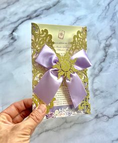 a hand holding up a card with a purple bow on the front and gold foil