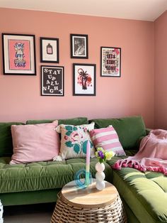 a living room with pink walls, green couches and pictures on the wall above