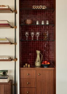 a wooden cabinet filled with lots of books and wine glasses next to a wall mounted book shelf