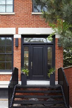 a black front door with two planters on the steps next to it and a brick building