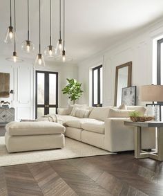 a living room filled with white furniture and lots of lights hanging from the ceiling above