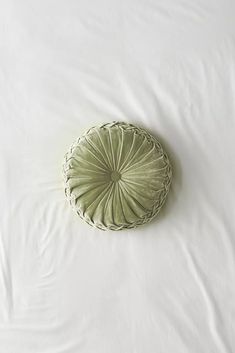 a white bed topped with a green pillow and a round shaped object on top of it