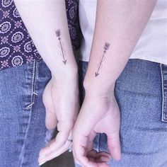 two people holding hands with tattoos on their arms and one has an arrow in the middle