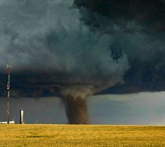 a large black cloud is in the sky over a field