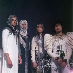 four men dressed in costume standing next to each other with flowers on their foreheads