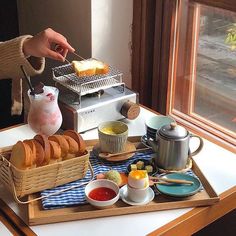 a tray with bread, cups and sauces on it next to a person holding a spoon